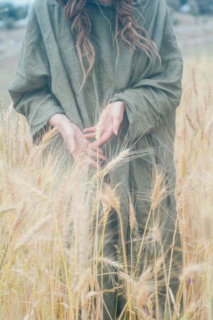 Woman in a green dress gently touching wheat in a golden field.