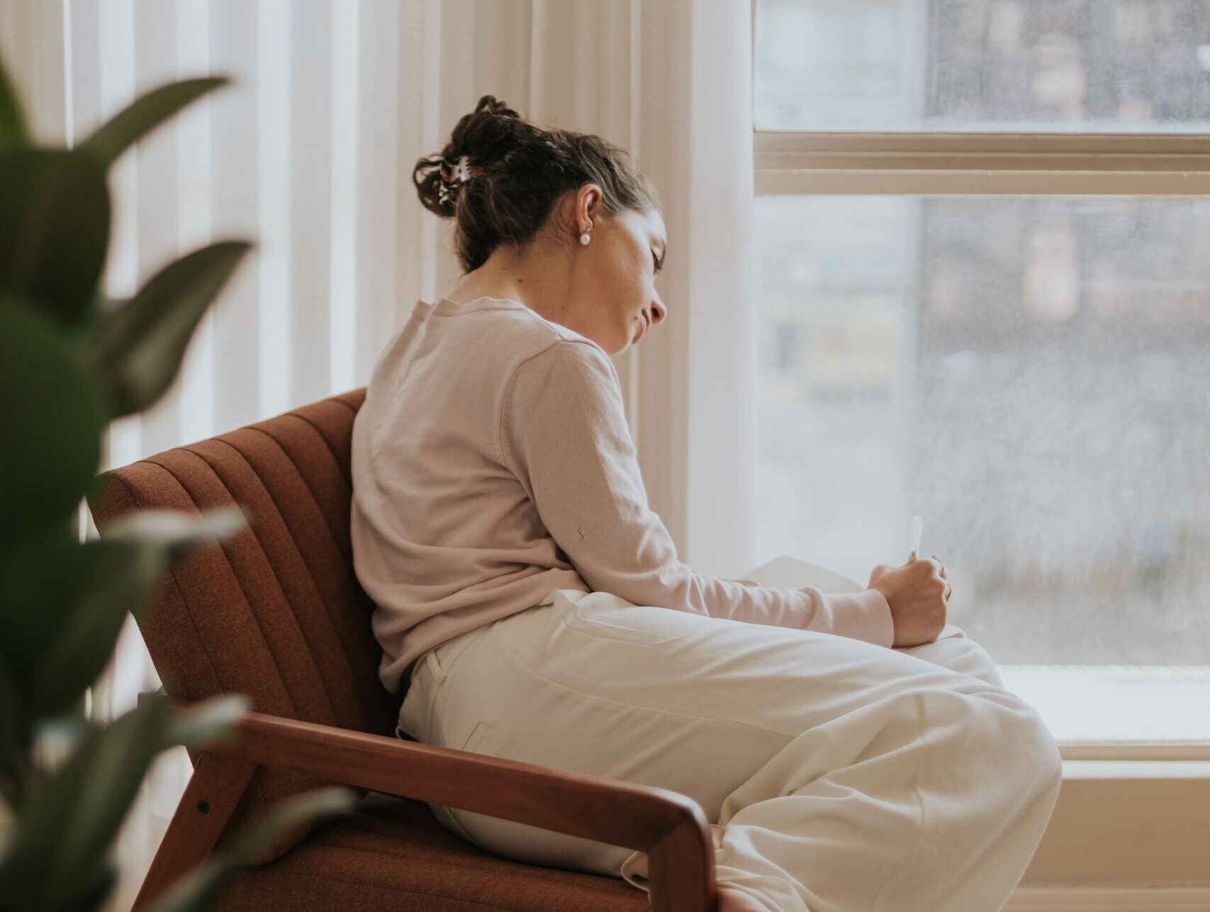 Woman relaxing on a chair by a window, deep in thought, indoors.